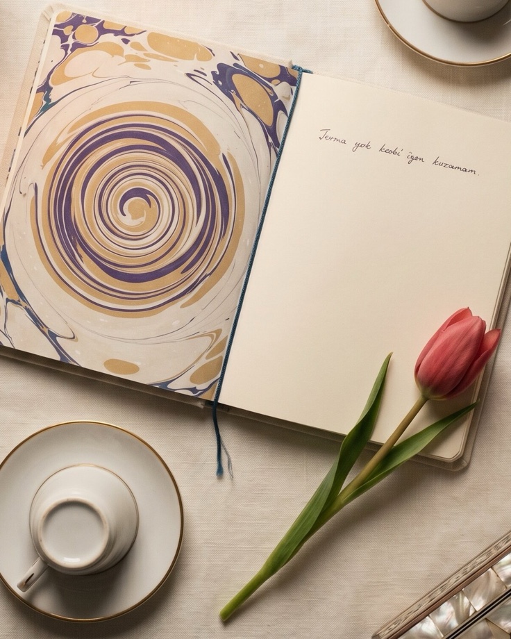 A marbled notebook open on linen, a tulip beside it and two cups